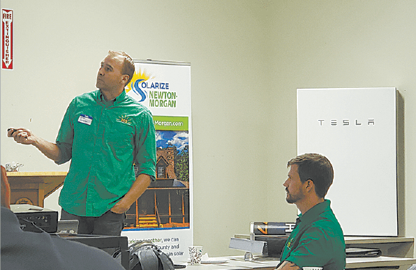 A member of the Alternative Energy Southeast, Inc. team giving a presentation as part of the Solarize Newton-Morgan campain with a Tesla Powerwall installed on the wall to the right